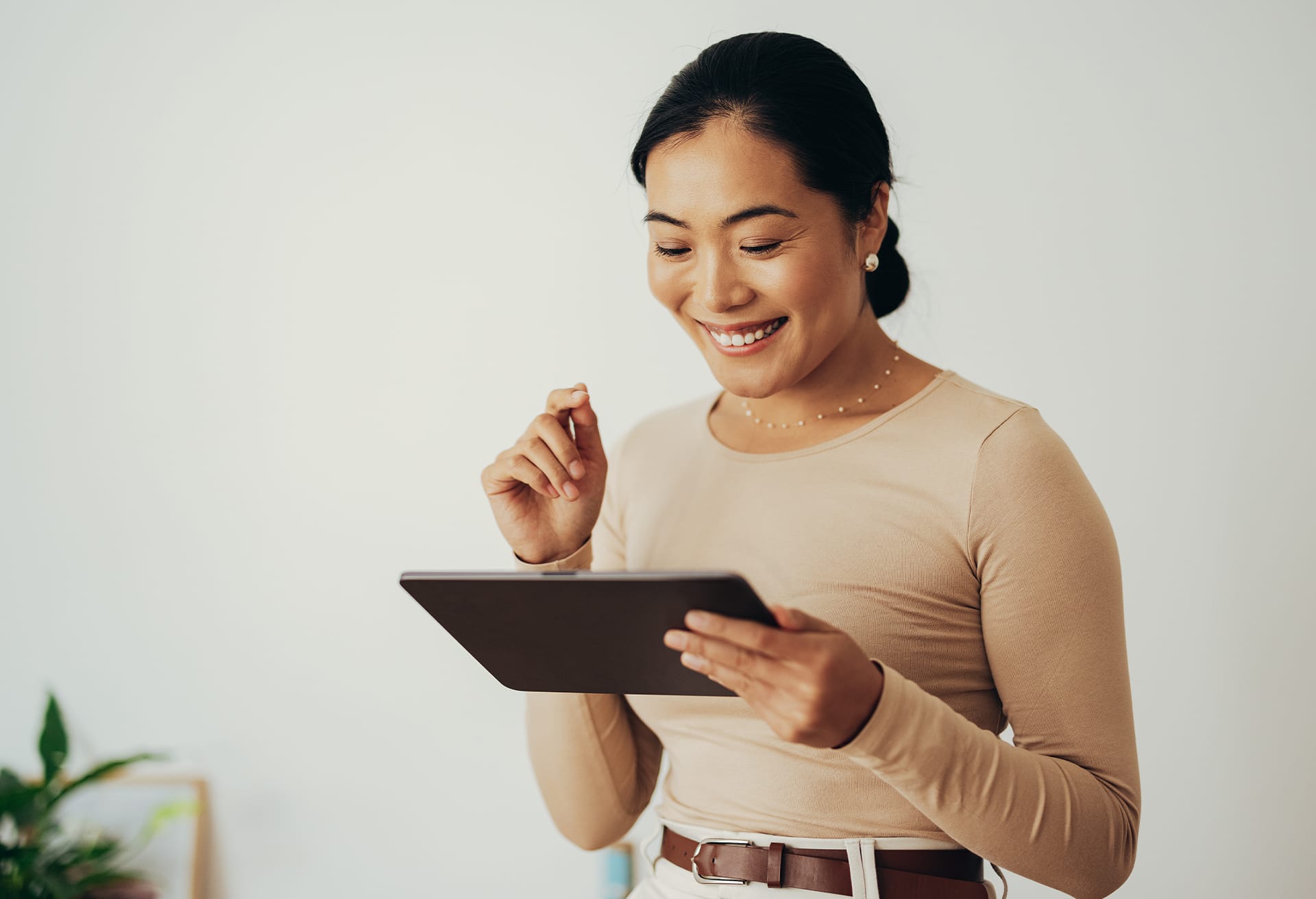 Smiling woman holding a tablet, looking at the screen with interest