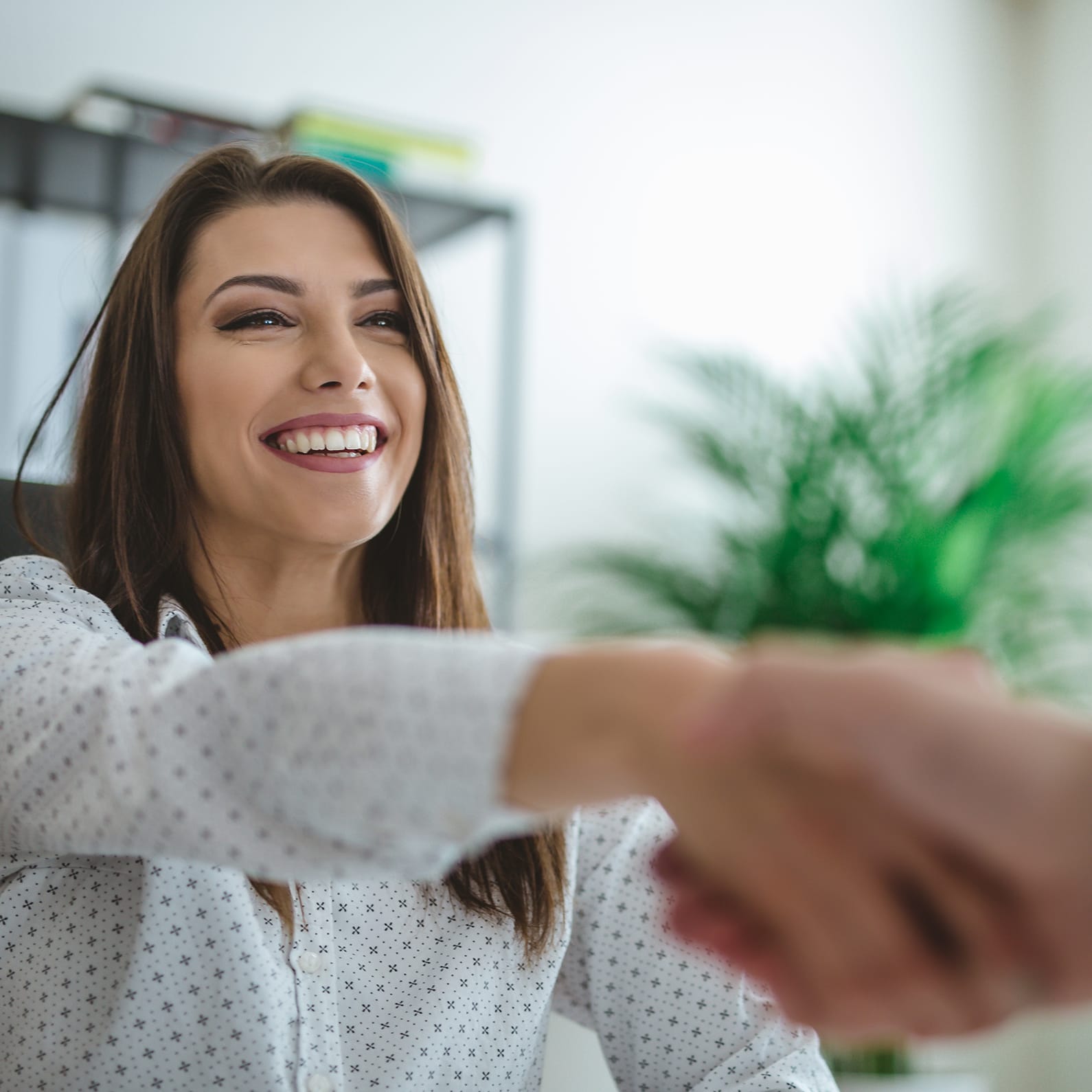 Smiling woman in a patterned shirt extends her hand for a handshake