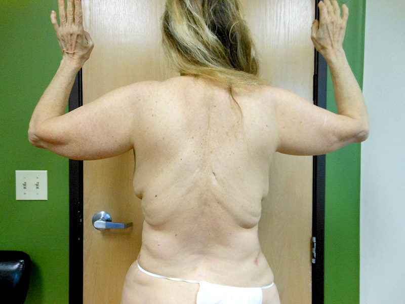 Back view of a person with long hair standing near a door, arms raised