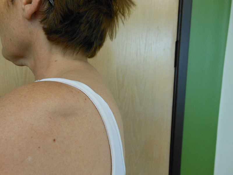 A person’s shoulder and neck, with a wooden wall and a green section behind them