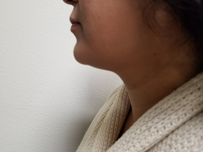 Profile of a woman with dark hair, wearing a light-colored sweater, against a plain wall